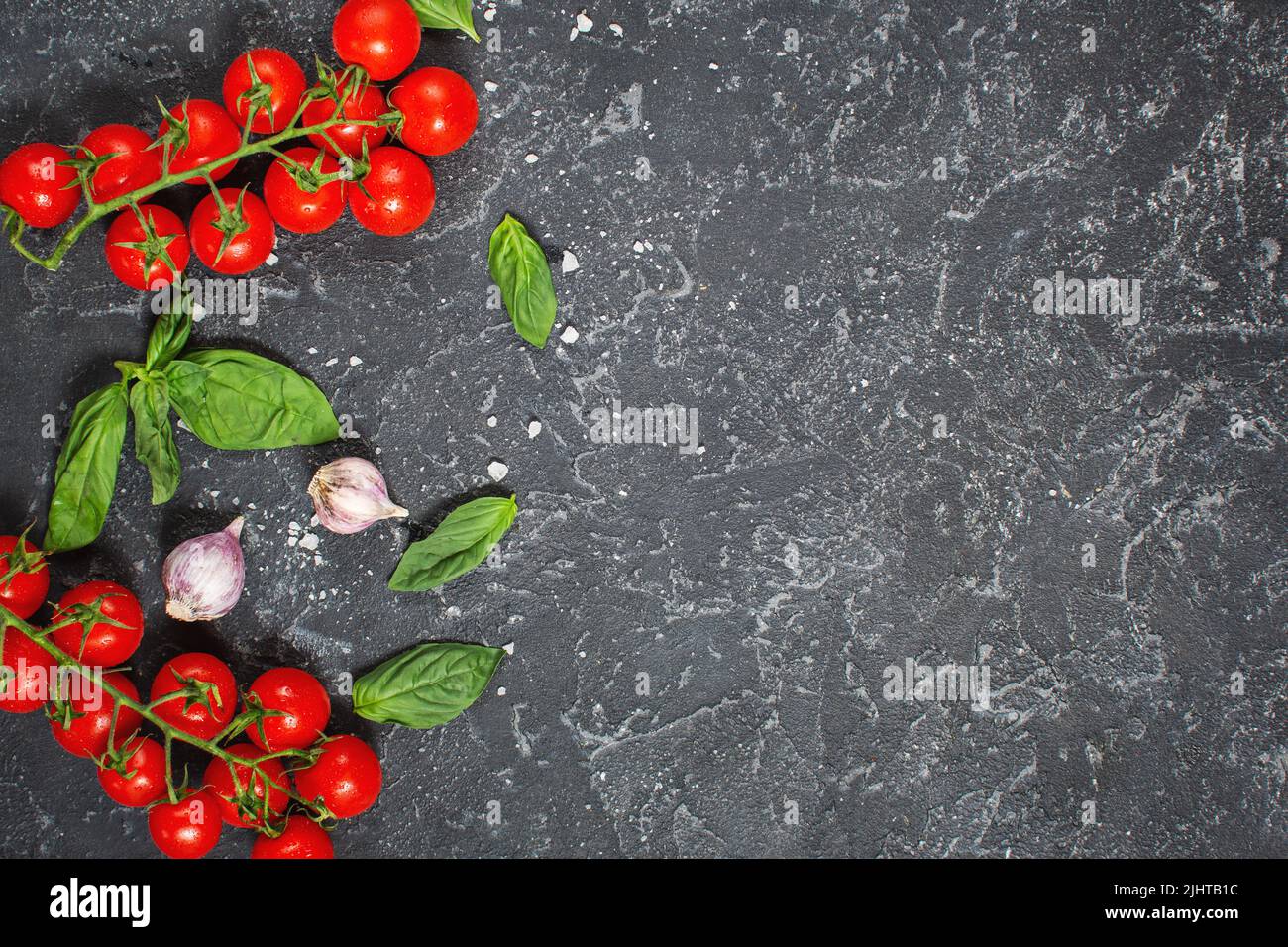 Fresh cherry tomatoes and basil with spices on a black stone background . Top view and copy space Stock Photo