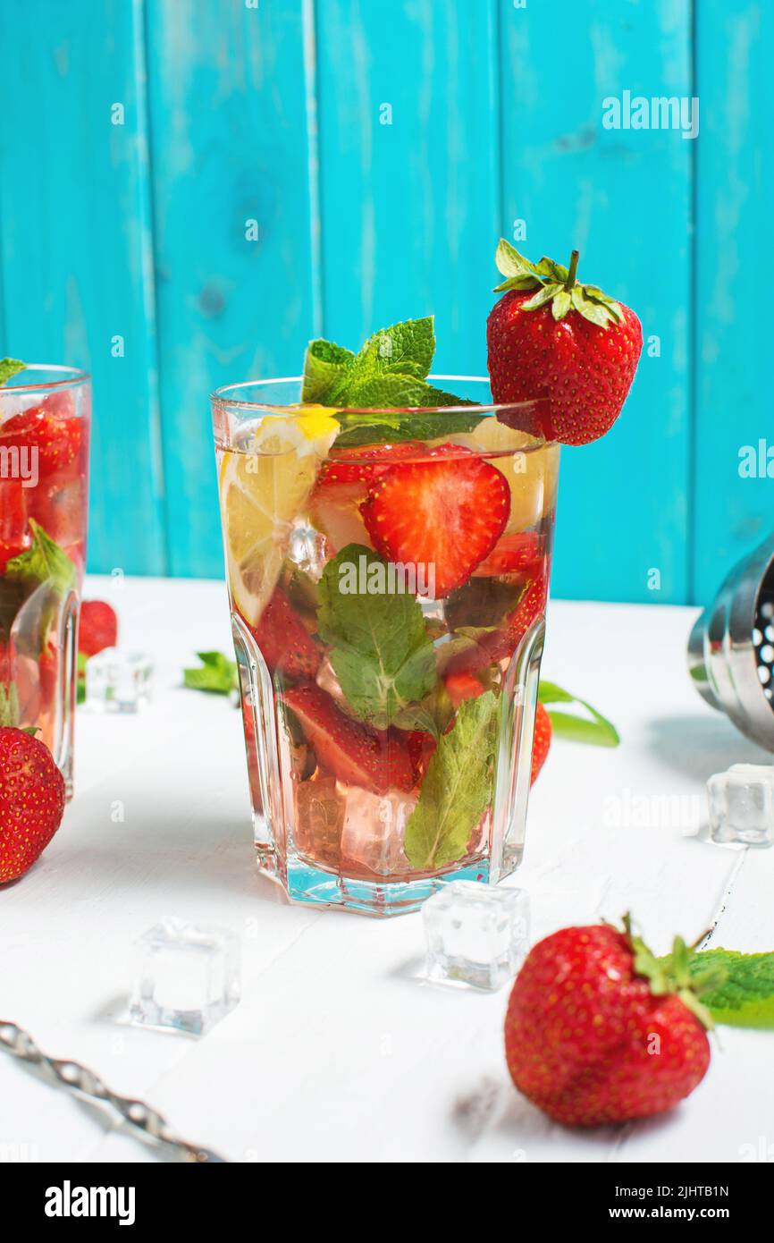 Summer refreshing mojito cocktail with strawberry, mint and lime with shaker for whipping drinks on a white wooden table Stock Photo
