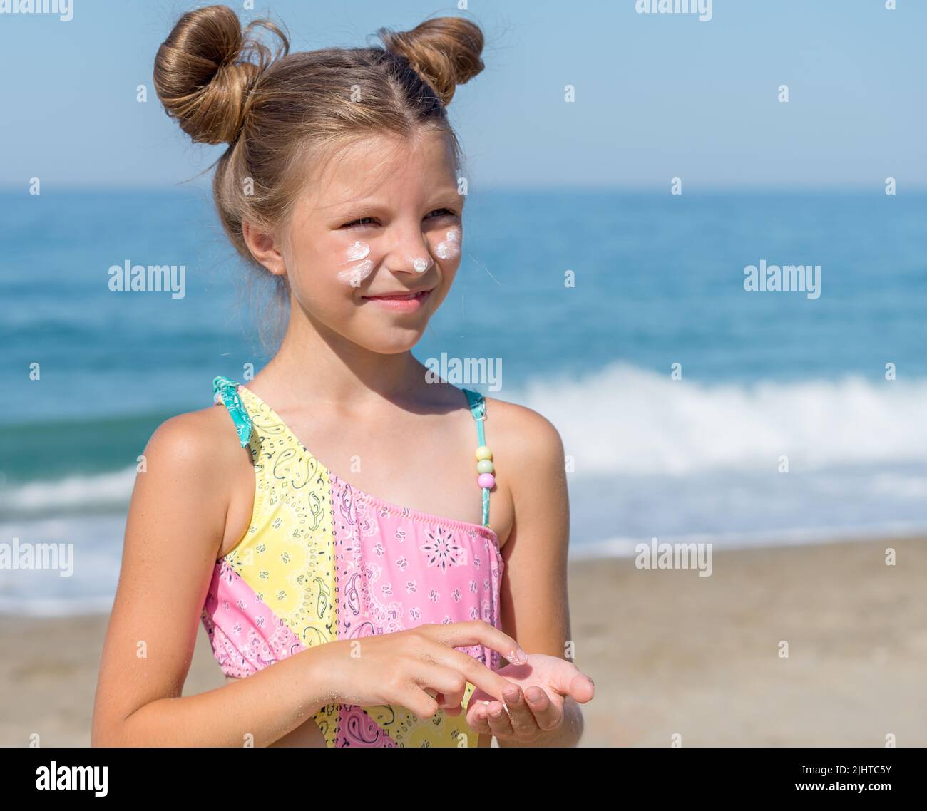 A young girl applies sunscreen to her body on the beach. Skin care