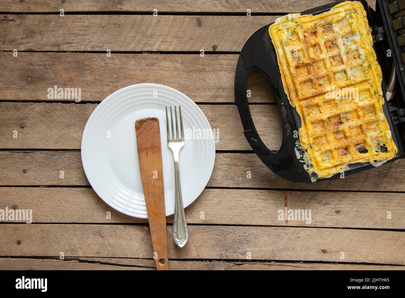 fry scrambled eggs with cheese and spices in a waffle iron on a wooden