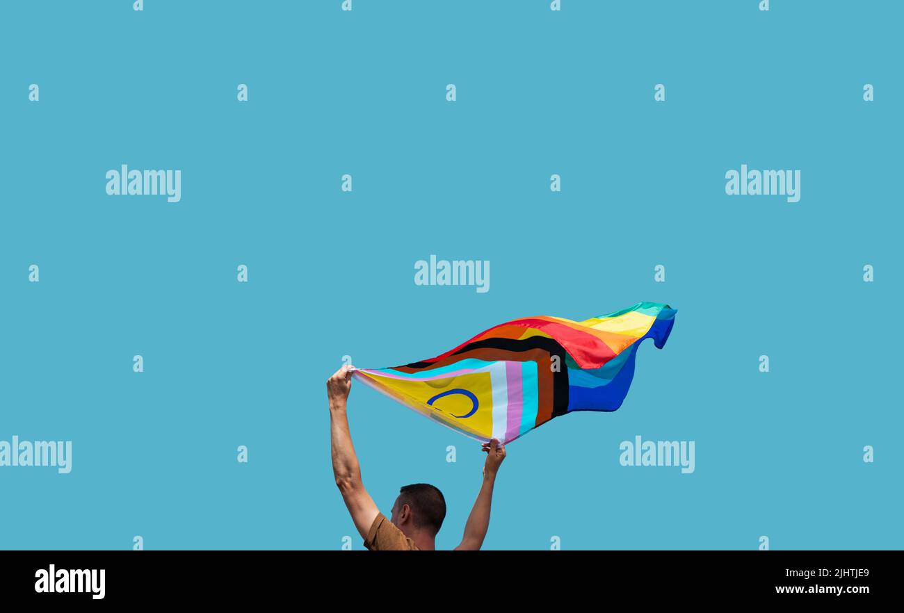 closeup of a man outdoors waving an intersex-inclusive progress pride flag above his head against the blue sky Stock Photo
