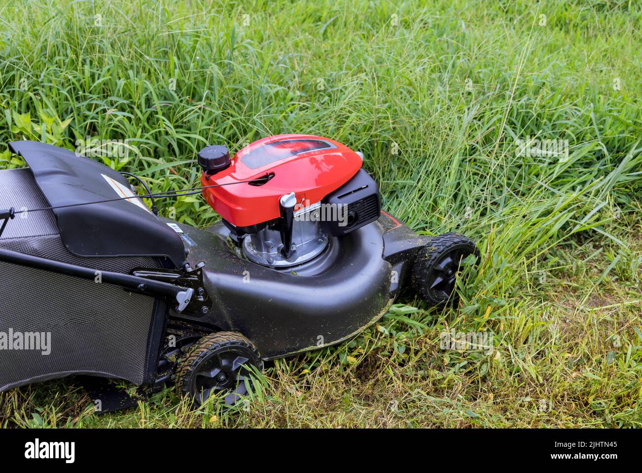 On a green lawn with grass cutting, a garden care tool is seen in the working lawn mower Stock Photo