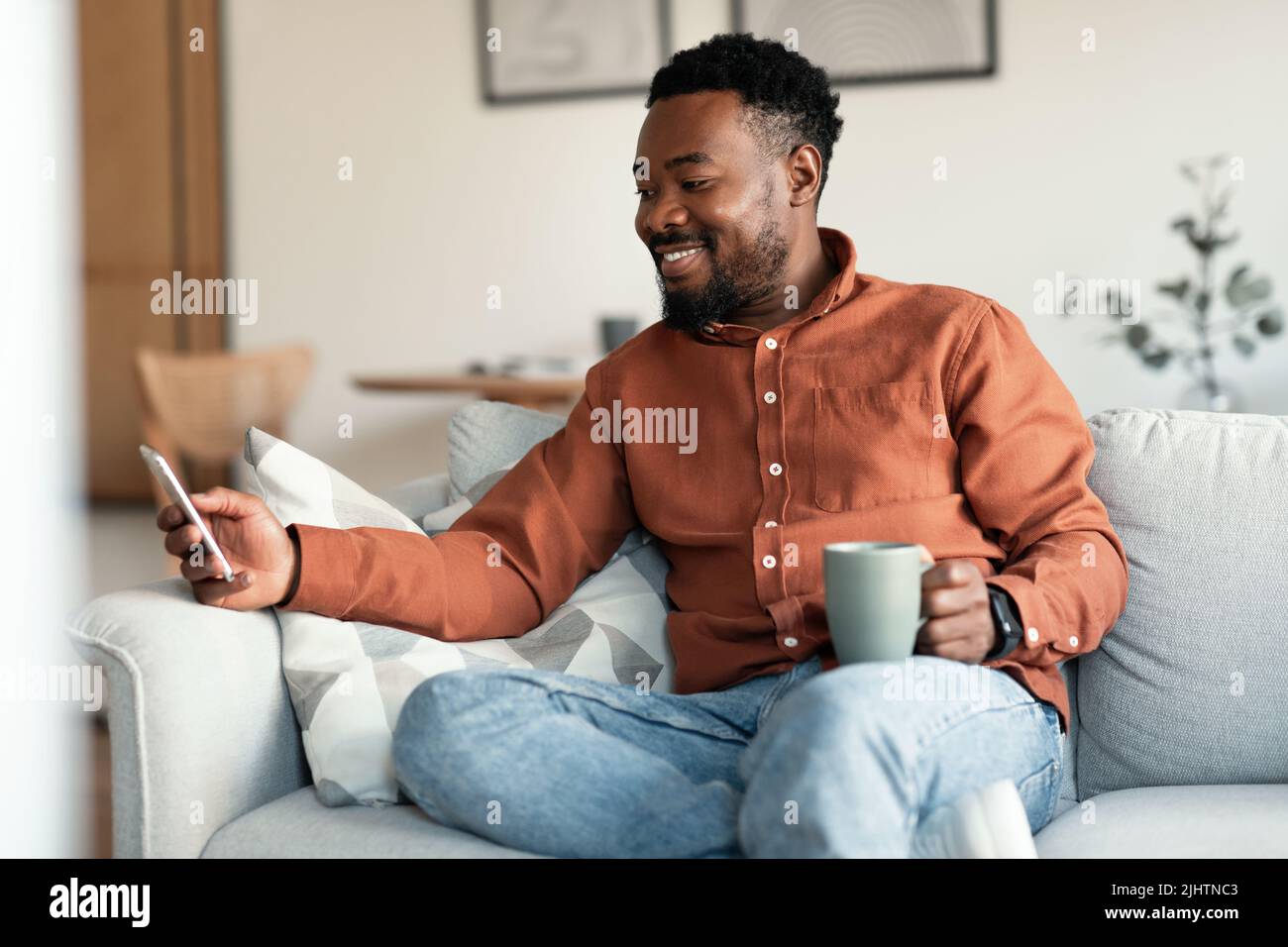 Happy Black Man Using Application On Smartphone Drinking Coffee Indoors Stock Photo