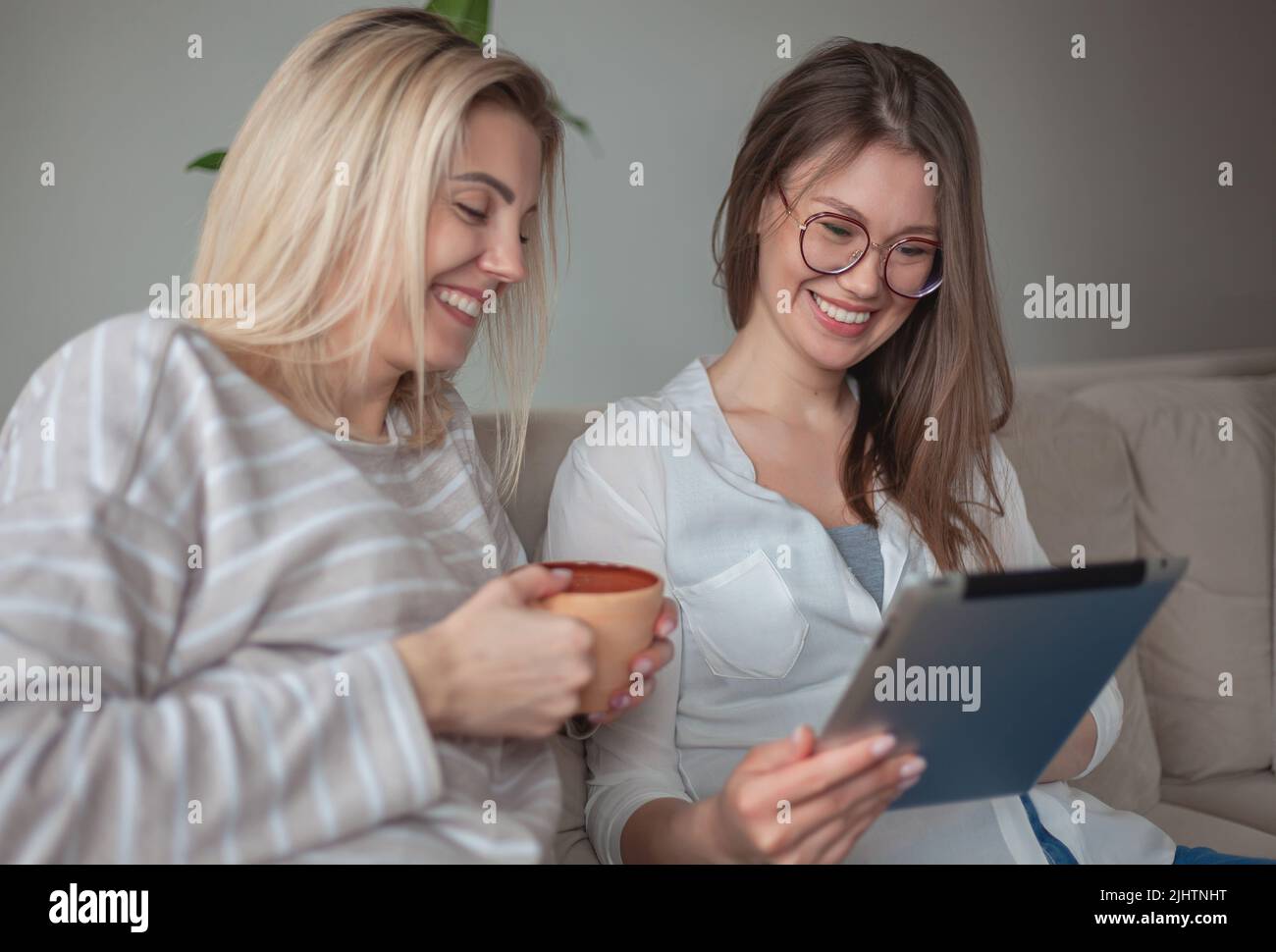 Two young women friends using tablet together, sitting on the co Stock Photo