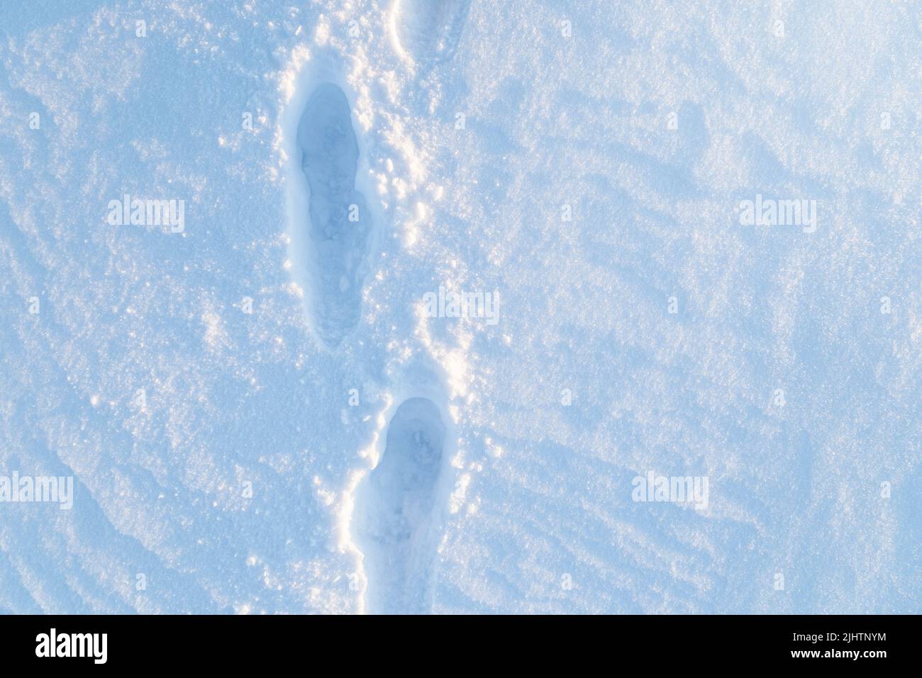 Fresh snowy ground with footsteps on a sunny day in the winter, viewed from above. Stock Photo