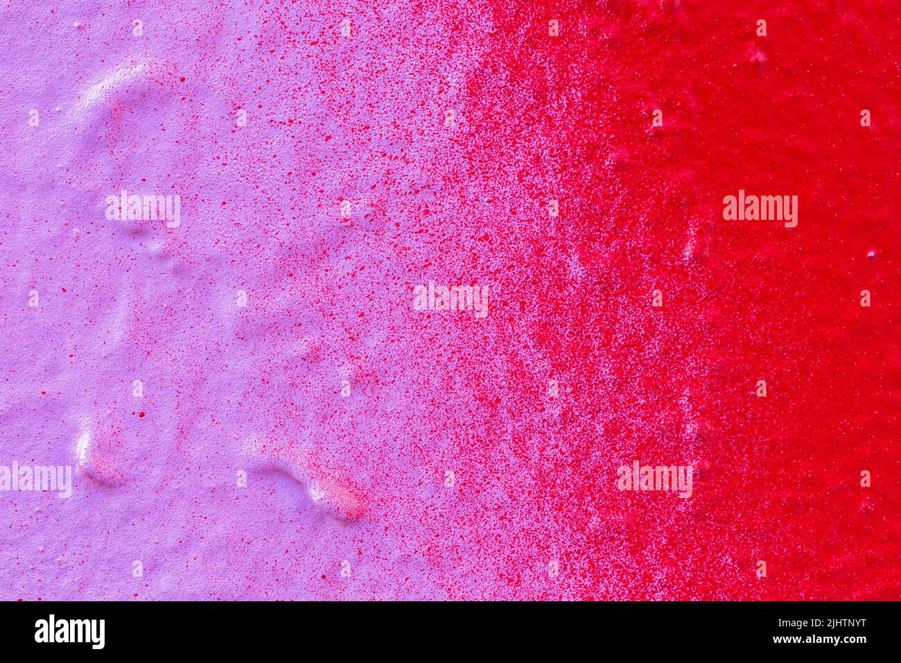 Macro close-up of a spray painted pink and red wall with splashes. Abstract full frame textured splattered graffiti background with copy space. Stock Photo
