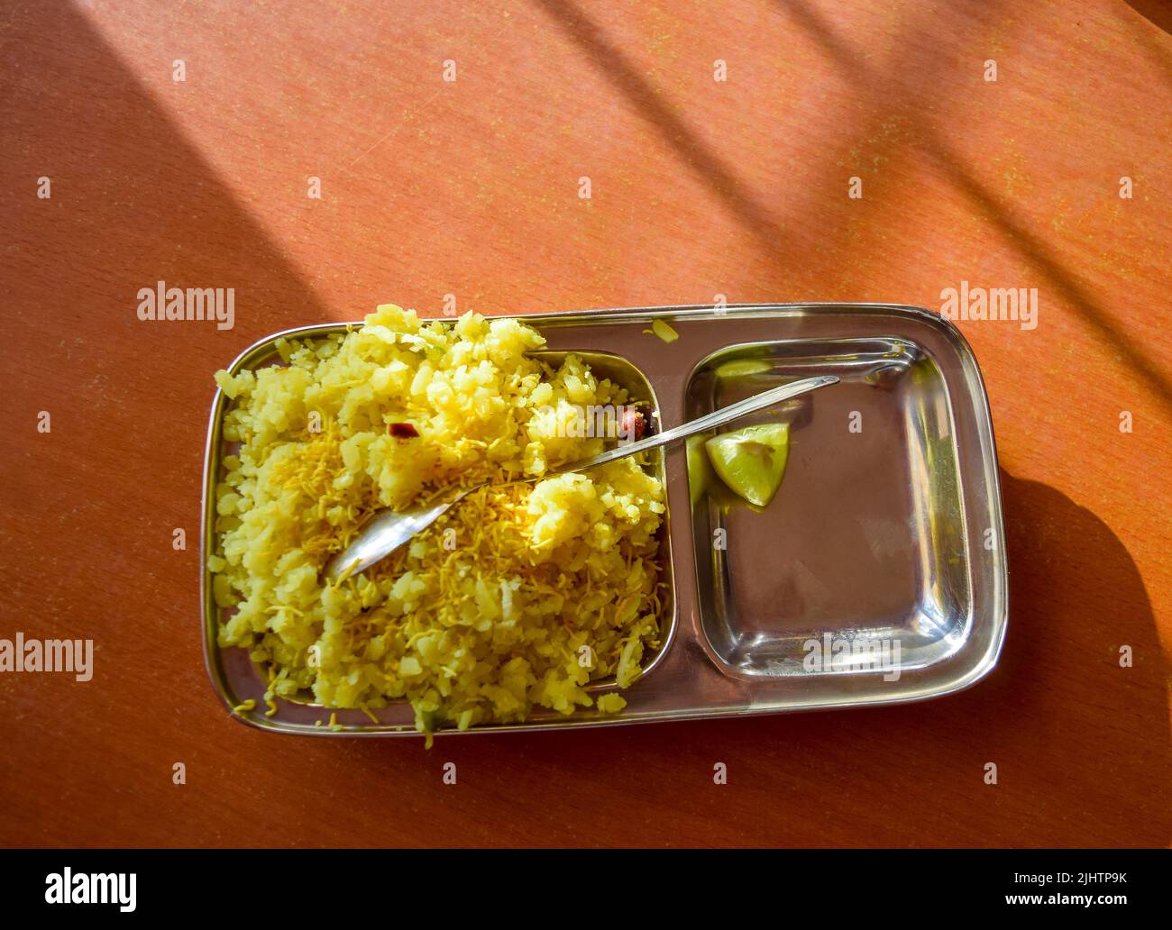 Poha with spoon in the plate with sunlight on the plate and on table ...