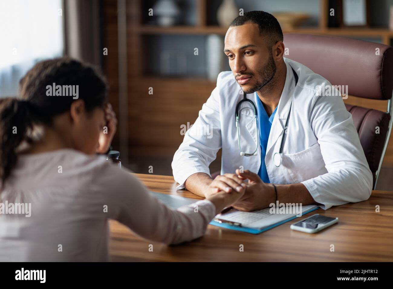 Doctor having conversation with upset black woman patient, holding hand ...