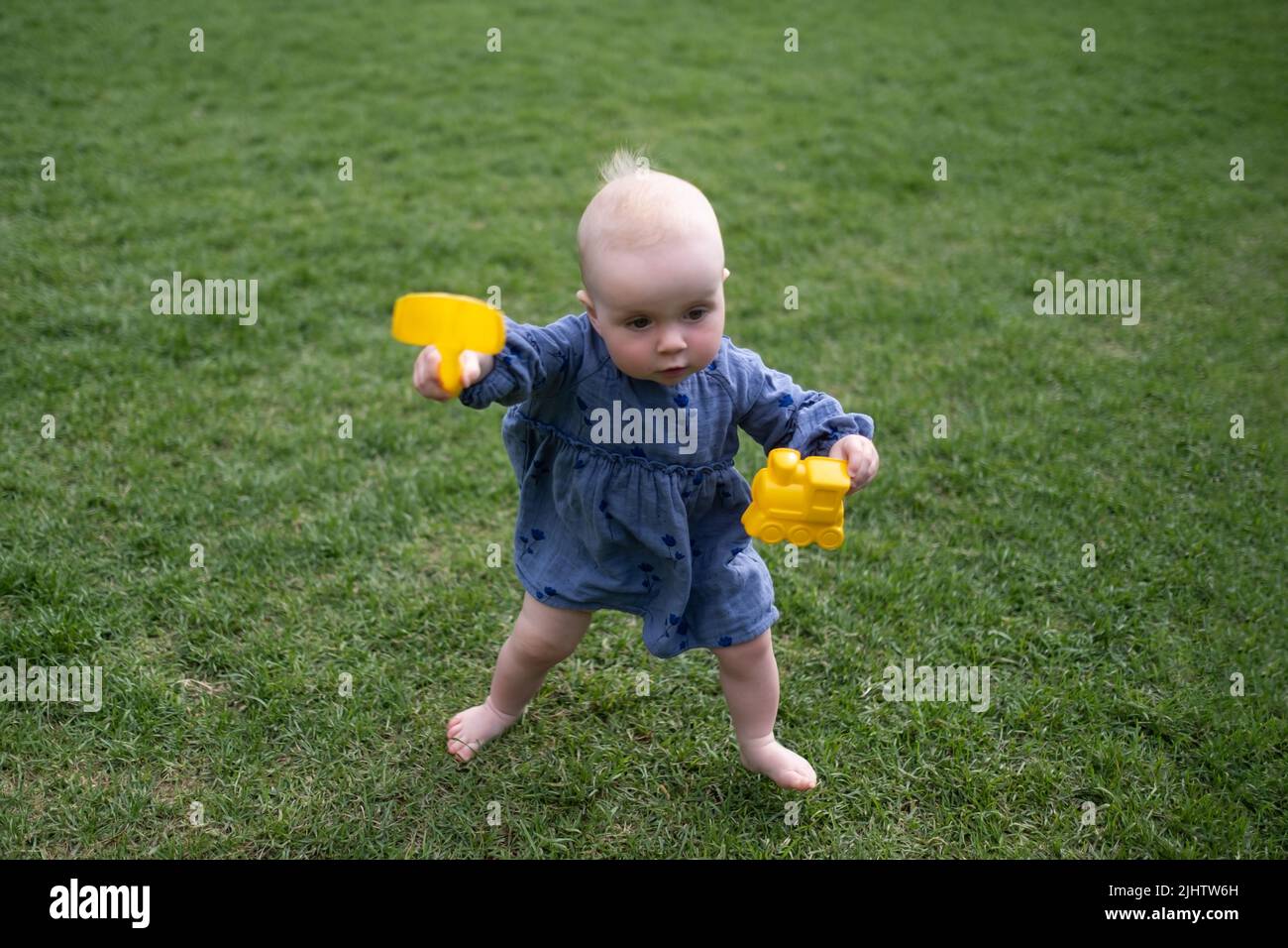 Happy child little girl study to go in the green lawn holding toys in hands. Stock Photo