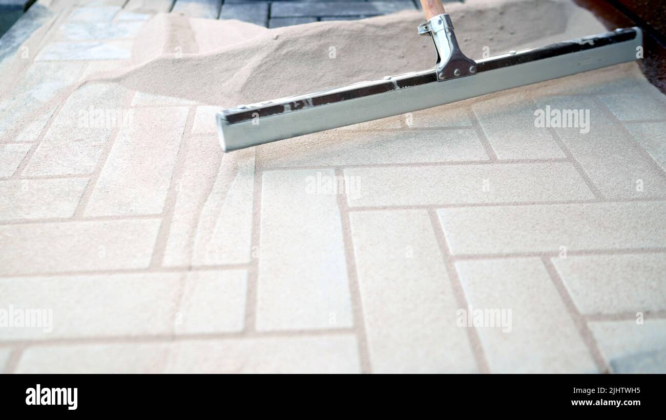 The principle of laying paving slabs. A worker spreads sand with a