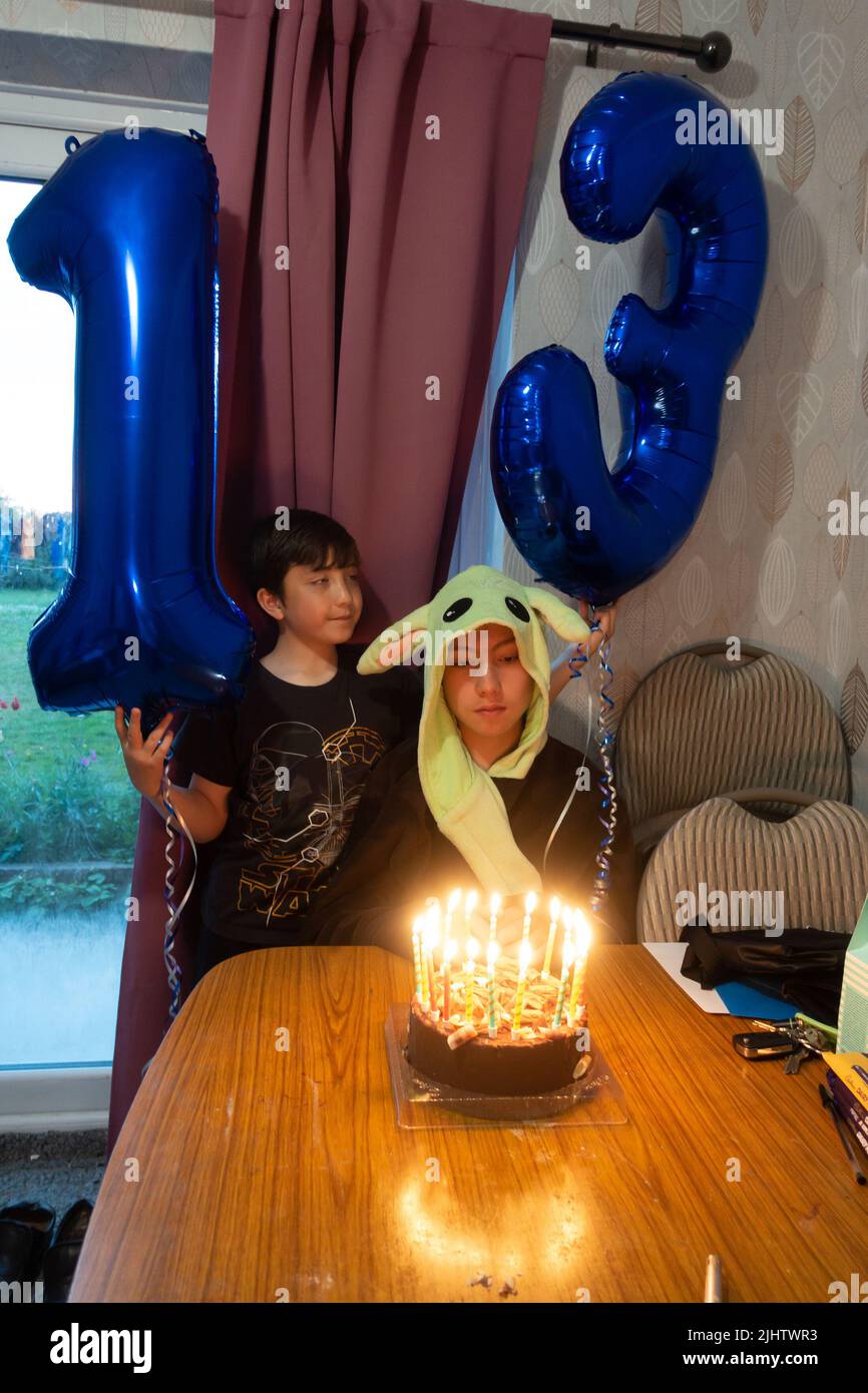 Celebrating a 13th birthday with helium filled foil balloons and a chocolate birthday cake with candles. Stock Photo