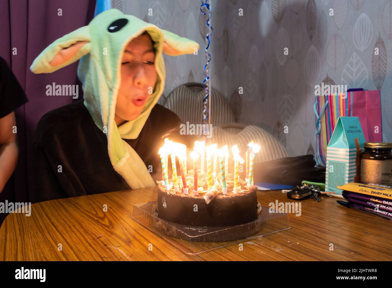 A boy blows out candles on a chocolate birthday cake while wearing a Yoda dressing gown. Stock Photo