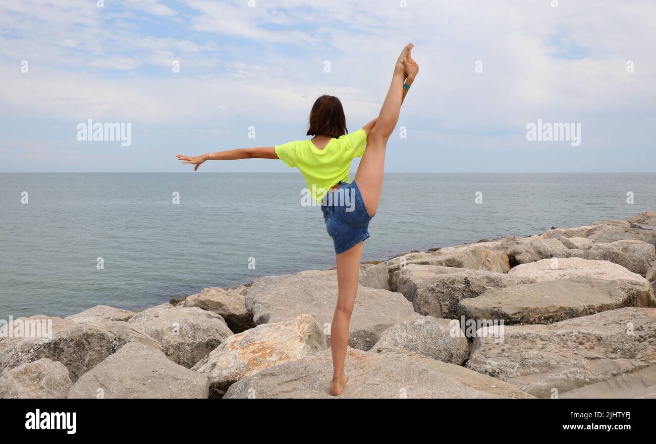 young girl does rhythmic gymnastics exercises on the rocks by the sea ...