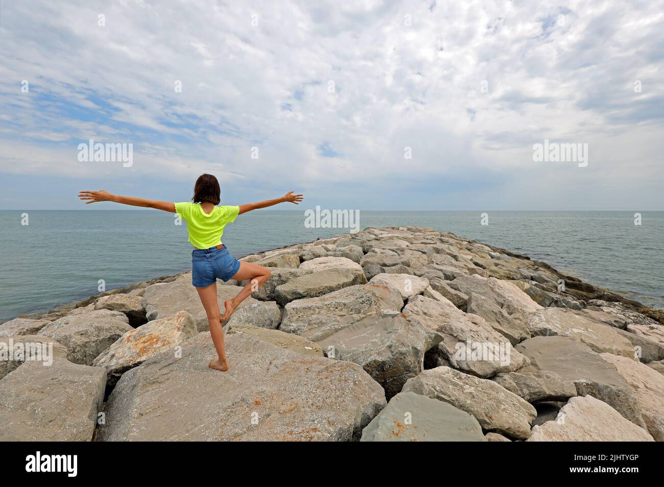 young girl does rhythmic gymnastics exercises on the rocks by the sea ...