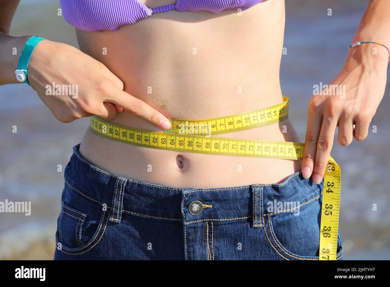 thin girl who measures her waist with the flexible measuring tape and shows her navel on her belly Stock Photo