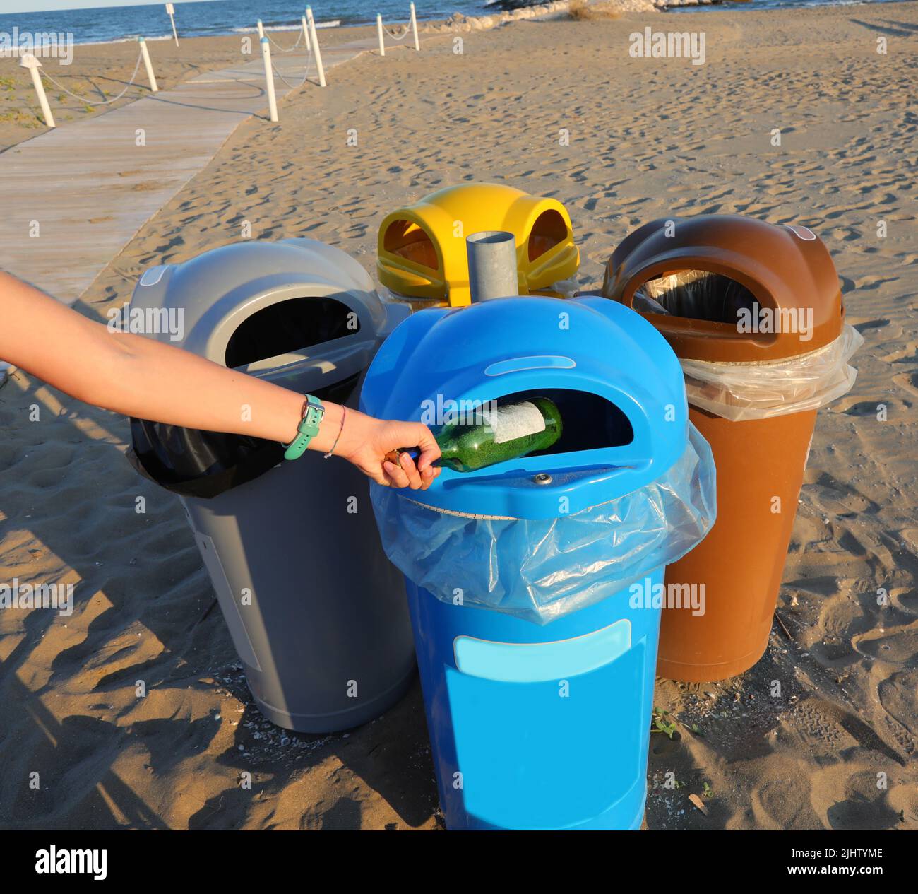 hand of the person throwing away a used glass bottle in the trash can