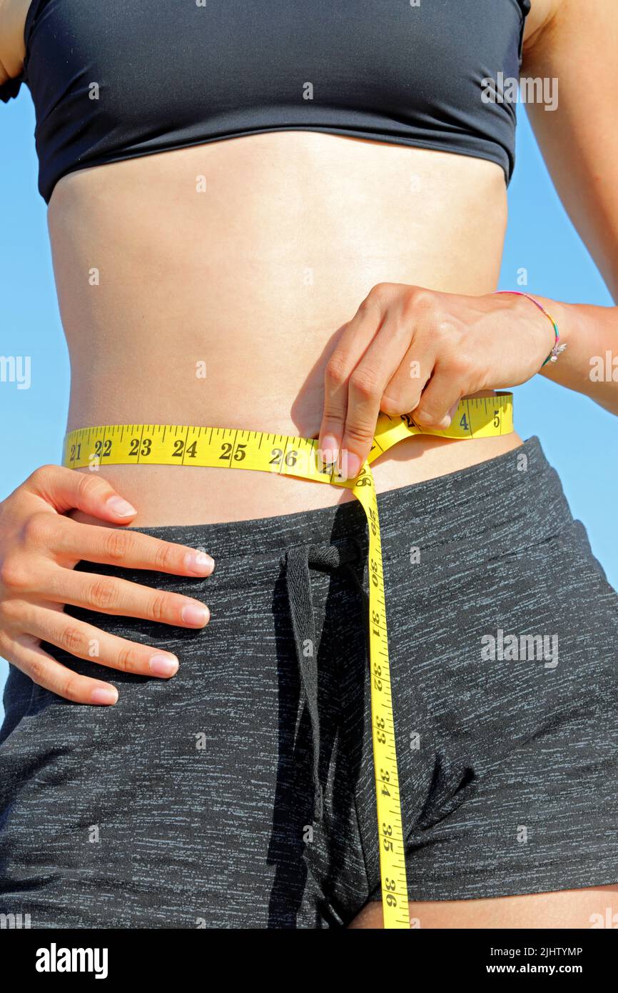 very slender girl measuring her waistline using a yellow measuring tape Stock Photo