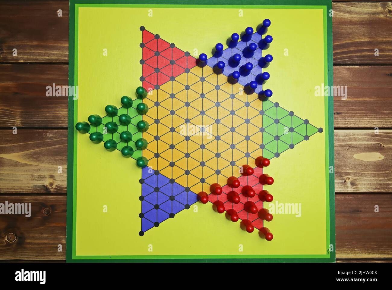 Top down view on isolated yellow gamboard with hexagon, multicolored game pieces, wooden background - chinese checkers (sternhalma) Stock Photo