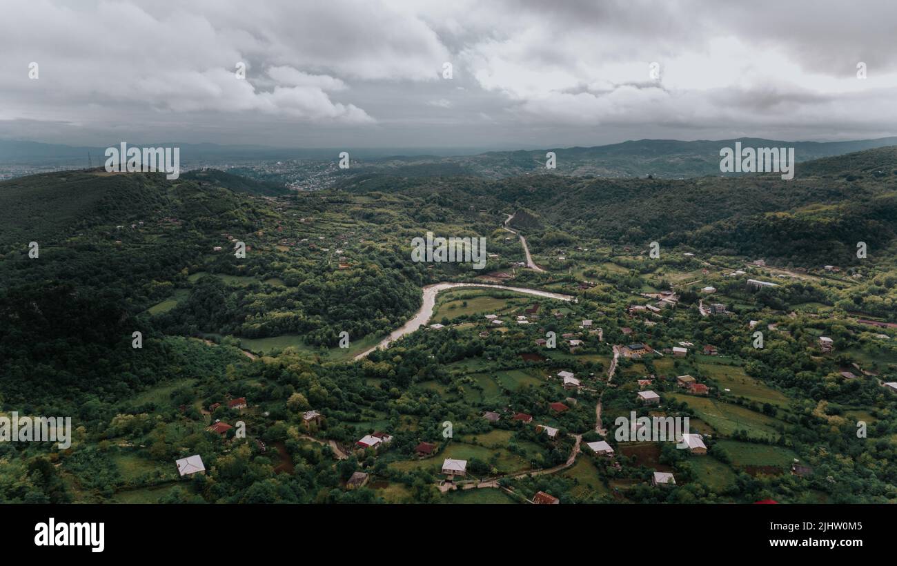 An aerial view of rural houses surrounded by green trees under a cloudy ...