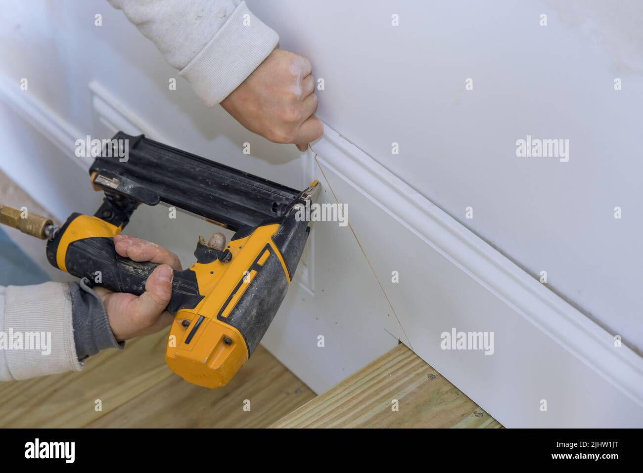 The carpenter uses a brad nail gun for the purpose of nailing the base