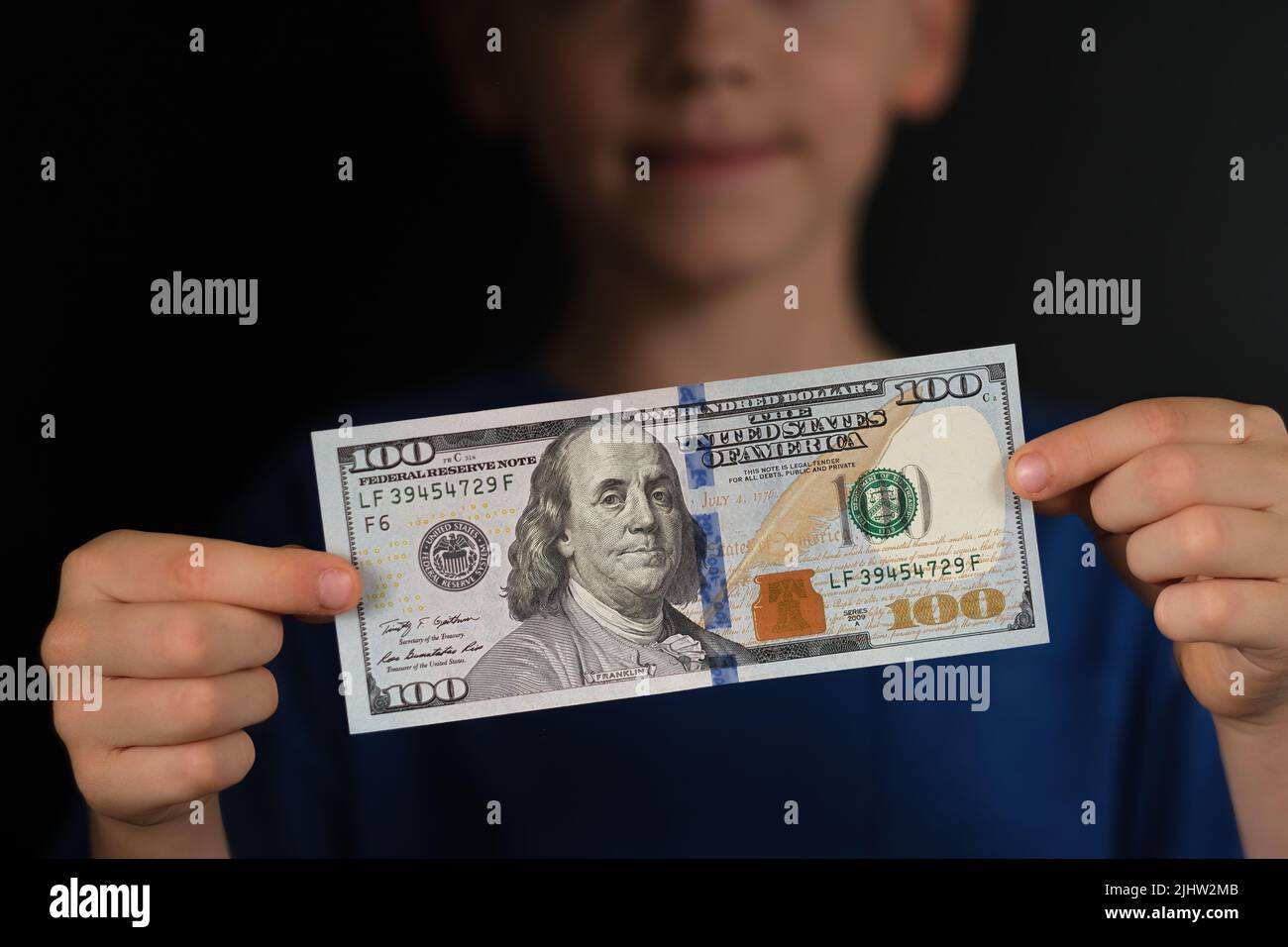 Banknote of one hundred US dollars seen in hands of a child. Concept for personal finance and children. Stock Photo