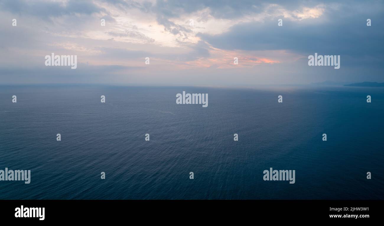 Sunrise color peaks through clouds over calm ocean landscape Stock Photo