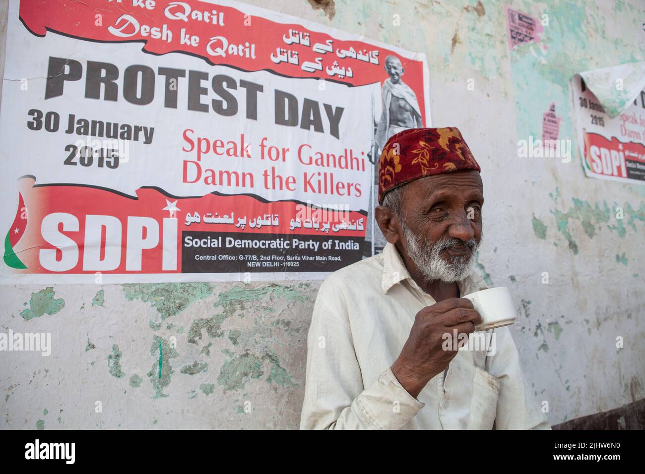 A man (blind in one eye) drinks a cup of tea in front of a SDPI political poster in Bijapur, India Stock Photo