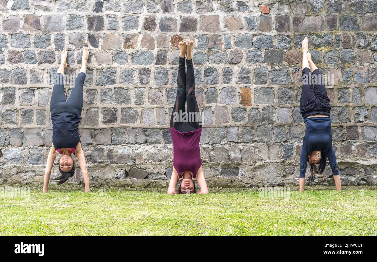Three women standing handstands on a wall practicing yoga in the morning outdoors Stock Photo
