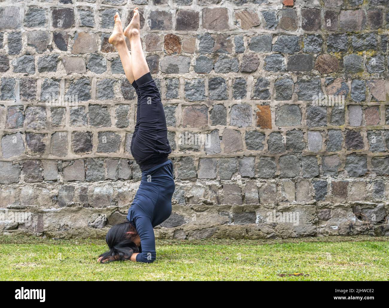 Young woman practicing headstand yoga in a park Stock Photo
