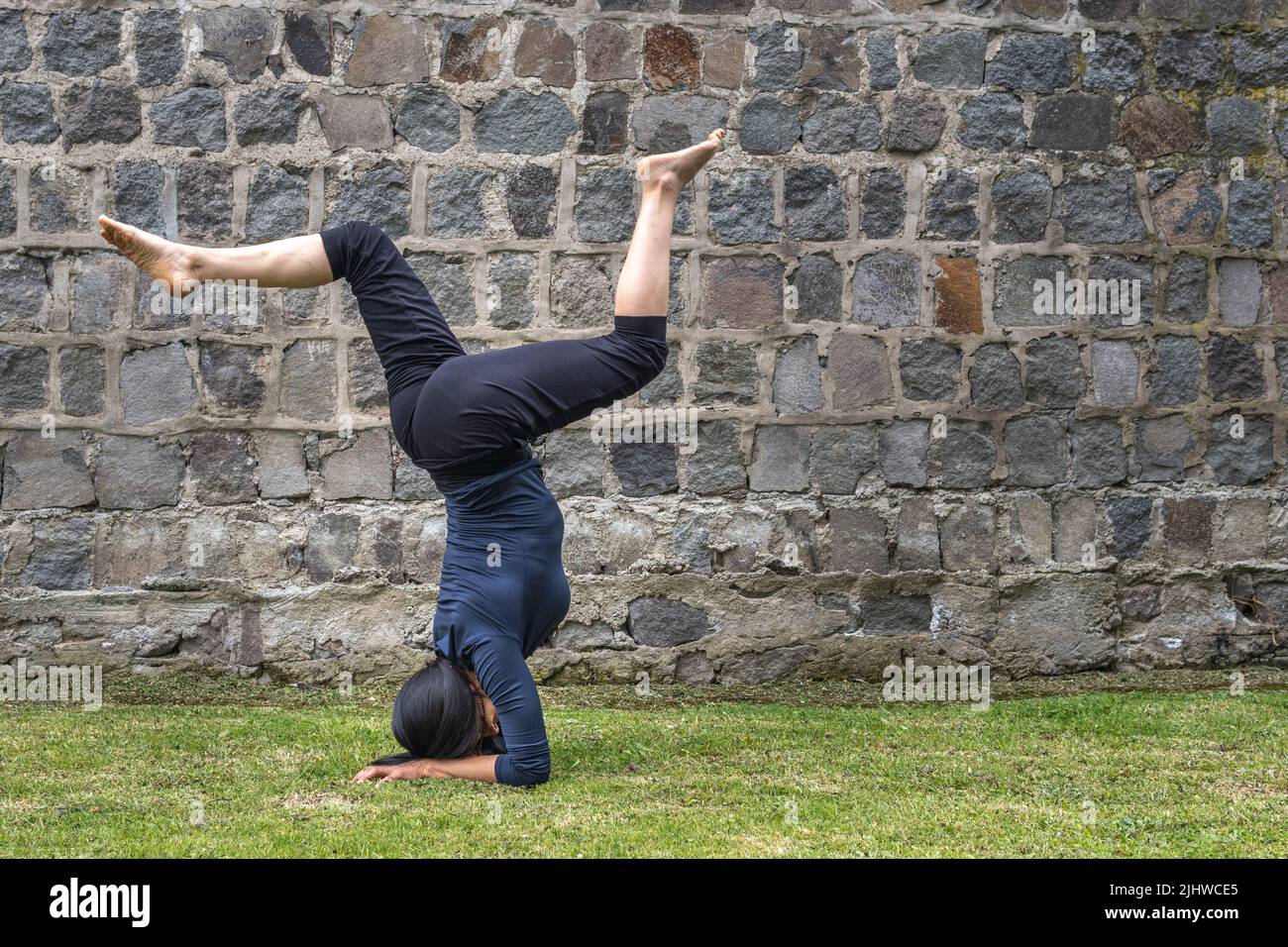 Mature woman performing yoga outdoors. Headstand posture with twisted leg Stock Photo