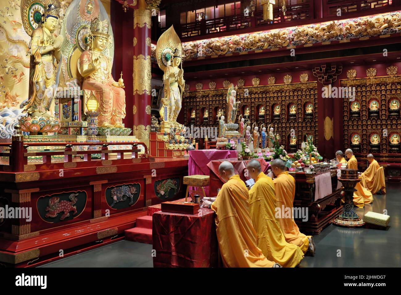 Yellow-robed Buddhist monks conducting prayers in the ornate prayer hall of Buddha Tooth Relic Temple and Museum in Chinatown, Singapore Stock Photo