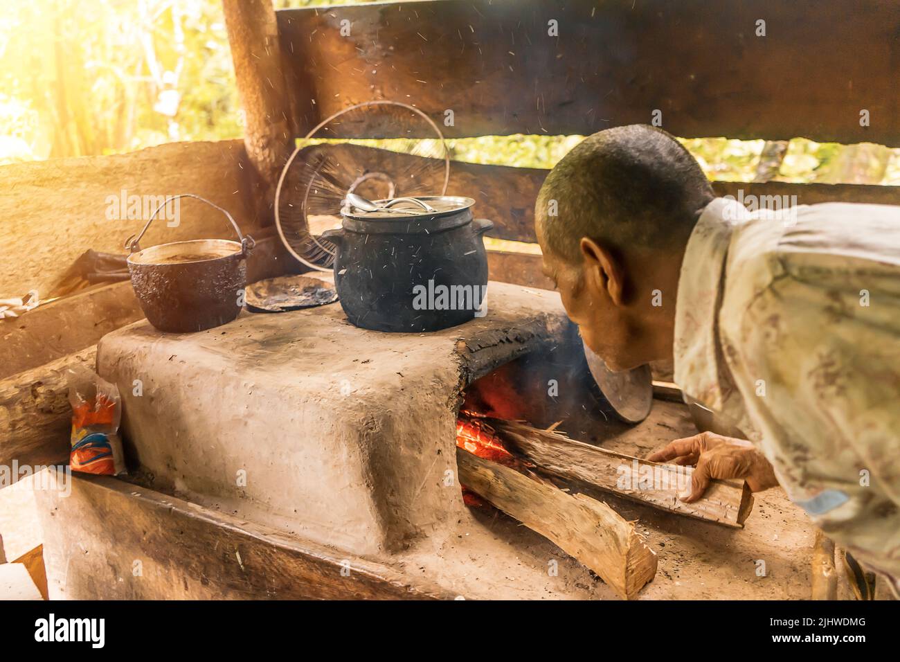 Latino grandfather stoking the fire to cook in his poor house Stock Photo