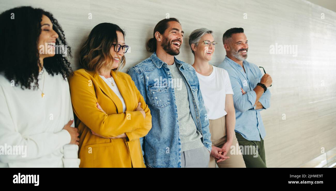 Successful business team laughing cheerfully while standing together against a wall. Group of multicultural businesspeople working together in a moder Stock Photo