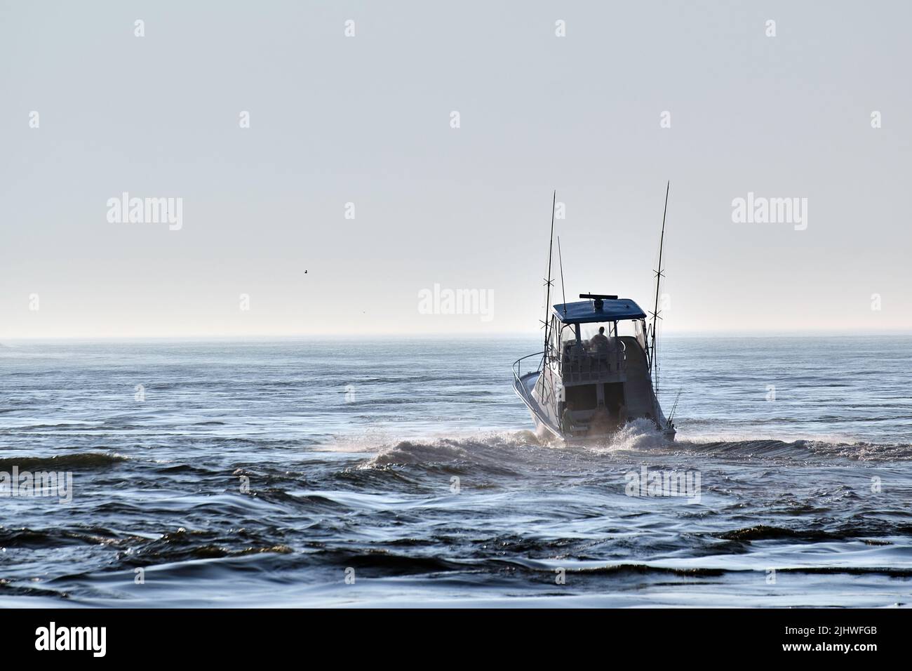 A private sport fishing boat heads through Indian River Inlet and  out into the Atlantic Ocean on a sunny, misty morning. Stock Photo