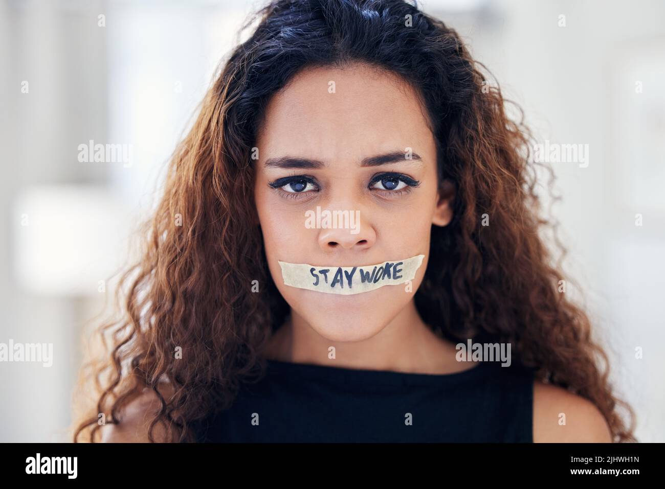 Its time to call out all forms of oppression and injustice. Portrait of a young woman with tape on her mouth that has the words stay woke written on Stock Photo