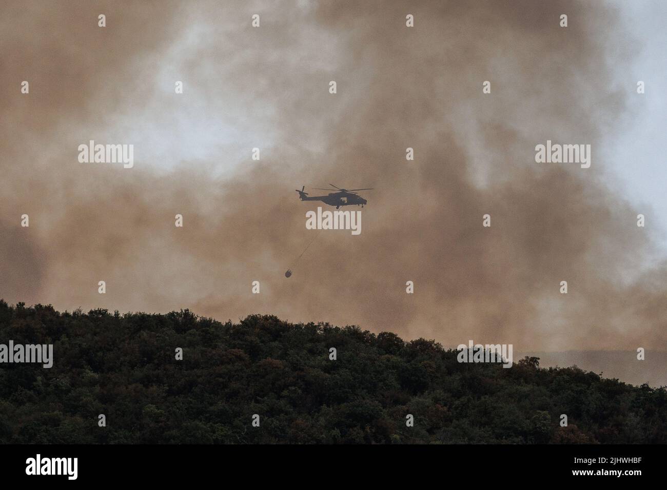 Trieste, Italy. 20th July, 2022. A helicopter carrying a bambi bucket for extinguishing fires flies through smoke as a large wildfire rages near Trieste. Wildfires have been breaking out in the region since Sunday when a large wildfire started just across the border in the Slovenian Karst region. (Photo by Luka Dakskobler/SOPA Images/Sipa USA) Credit: Sipa USA/Alamy Live News Stock Photo