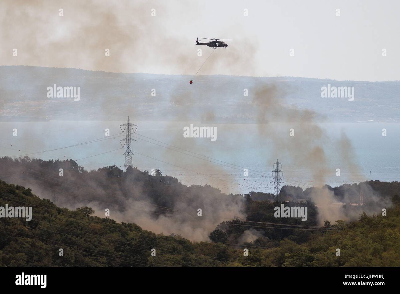 Trieste, Italy. 20th July, 2022. A helicopter carrying a bambi bucket for extinguishing fires flies through smoke as a large wildfire rages near Trieste. Wildfires have been breaking out in the region since Sunday when a large wildfire started just across the border in the Slovenian Karst region. Credit: SOPA Images Limited/Alamy Live News Stock Photo