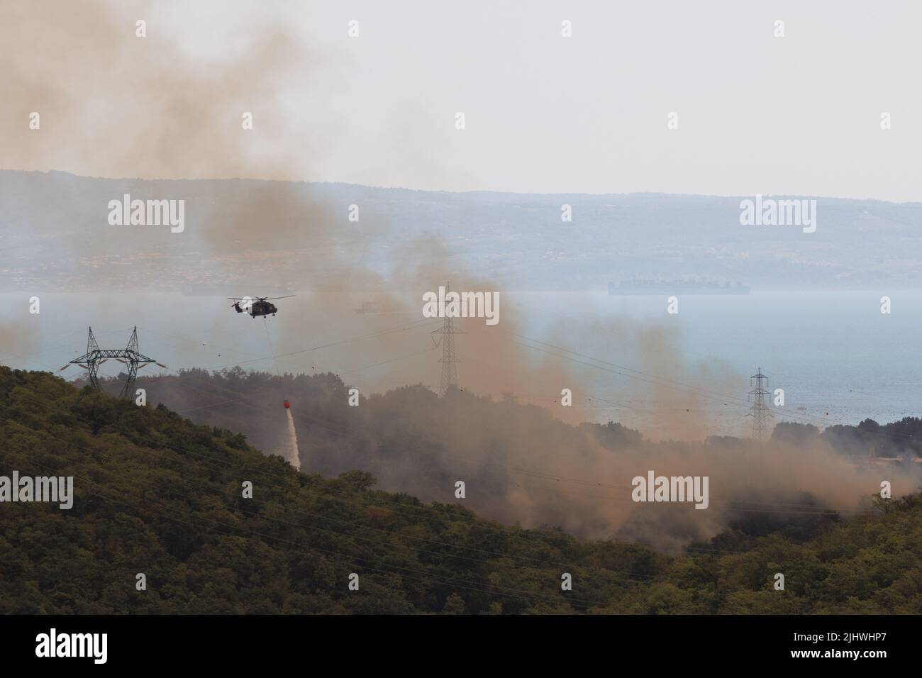 Trieste, Italy. 20th July, 2022. A helicopter carrying a bambi bucket for extinguishing fires drops water on a large wildfire that rages near Trieste. Wildfires have been breaking out in the region since Sunday when a large wildfire started just across the border in the Slovenian Karst region. Credit: SOPA Images Limited/Alamy Live News Stock Photo