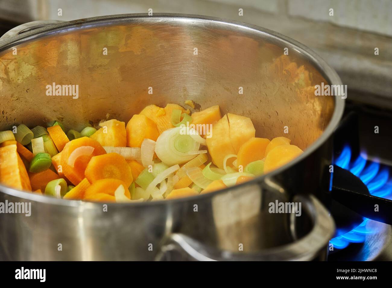 Onions, carrots and leeks in pot on fire on gas stove Stock Photo Alamy