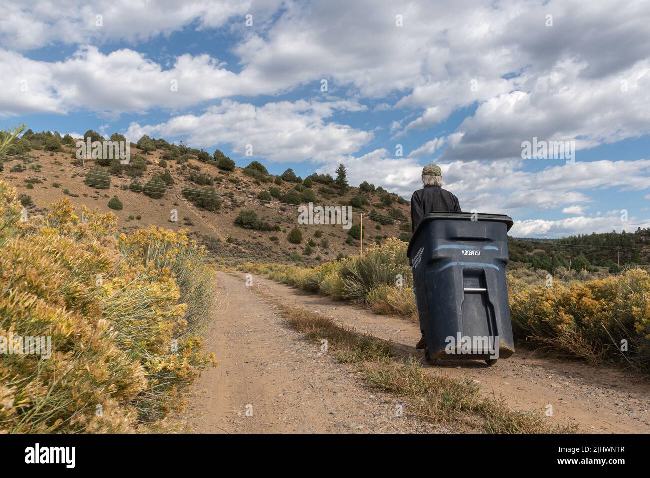 https://c8.alamy.com/comp/2JHWNTR/a-man-rolls-a-large-black-garbage-can-down-a-gravel-road-in-rural-new-mexico-united-states-2JHWNTR.jpg