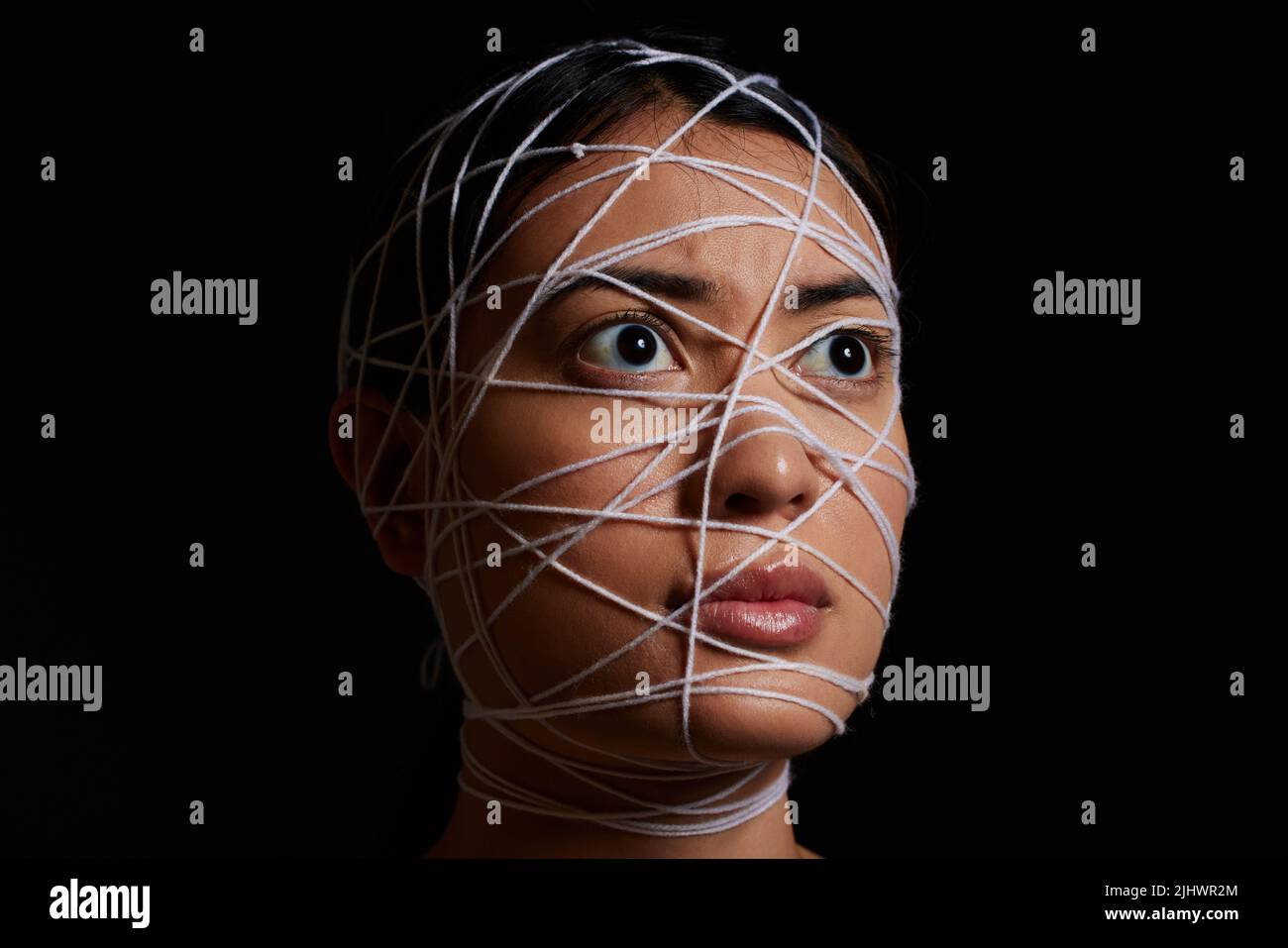 Helpless and afraid. a young woman wrapped in string against a dark background. Stock Photo