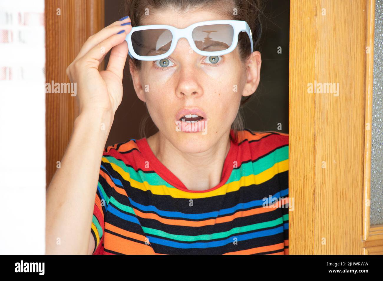 The girl's face looks with surprised eyes through the glasses, the emotion of surprise and surprise on the face of the maid Stock Photo