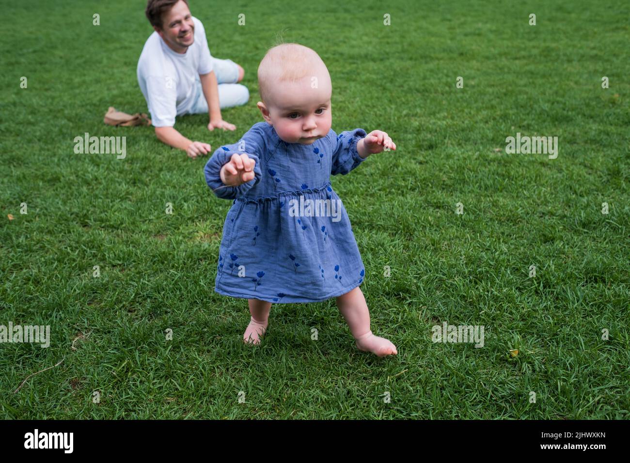 Happy child little girl study to go in the green lawn holding toys in hands. Stock Photo