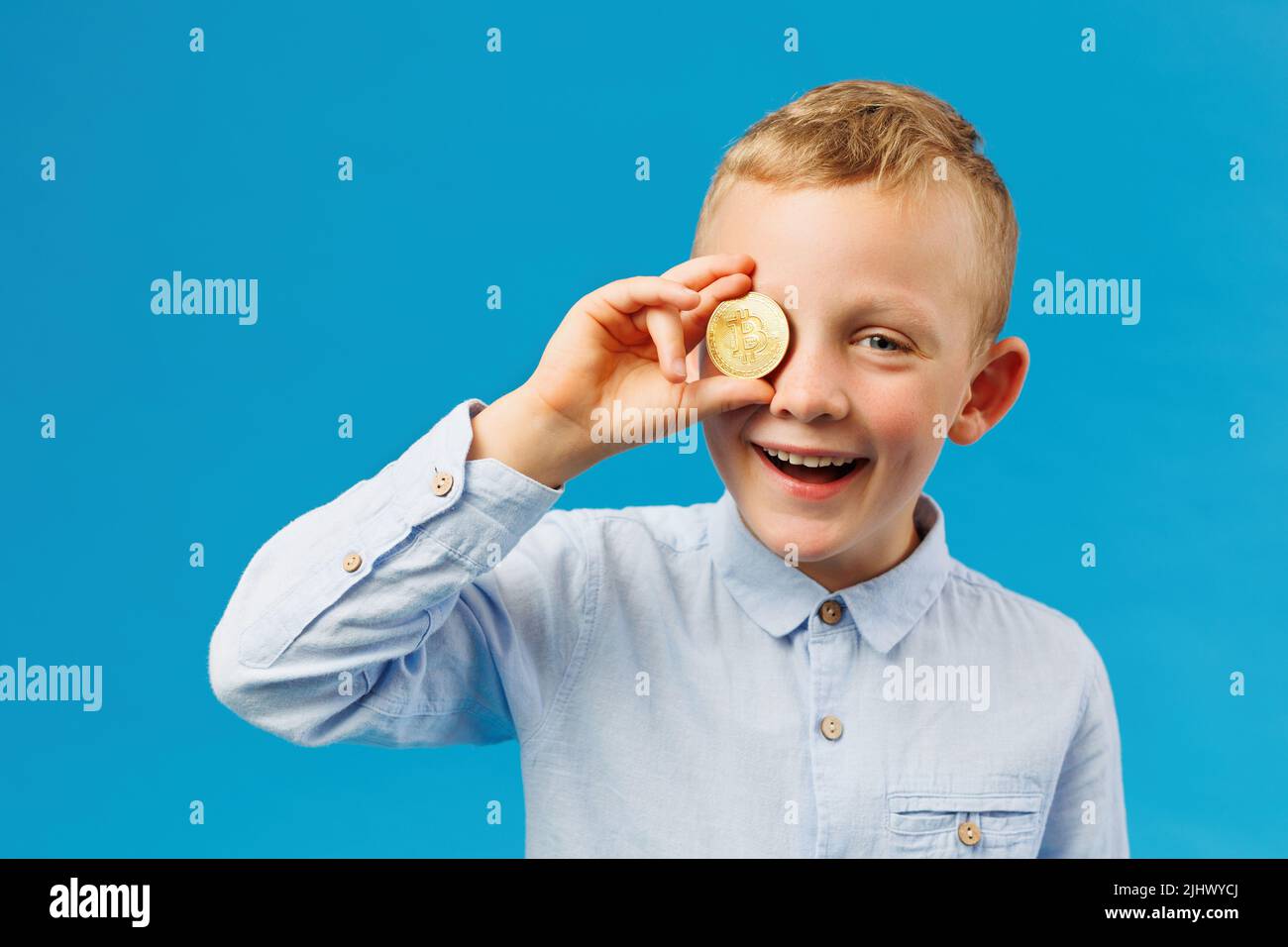 Cryptocurrency and modern finance. Cheerful boy holding golden bitcoin in  studio on the blue background and covers his eye with a coin Stock Photo -  Alamy