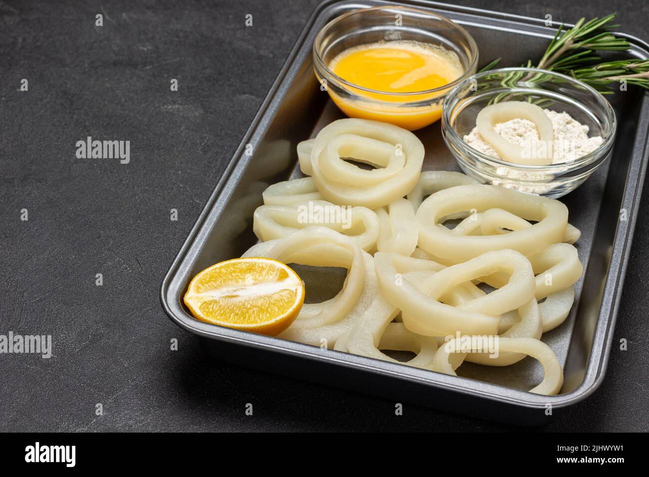 Squid cut into rings in baking tray. Flour and beaten raw egg in bowls