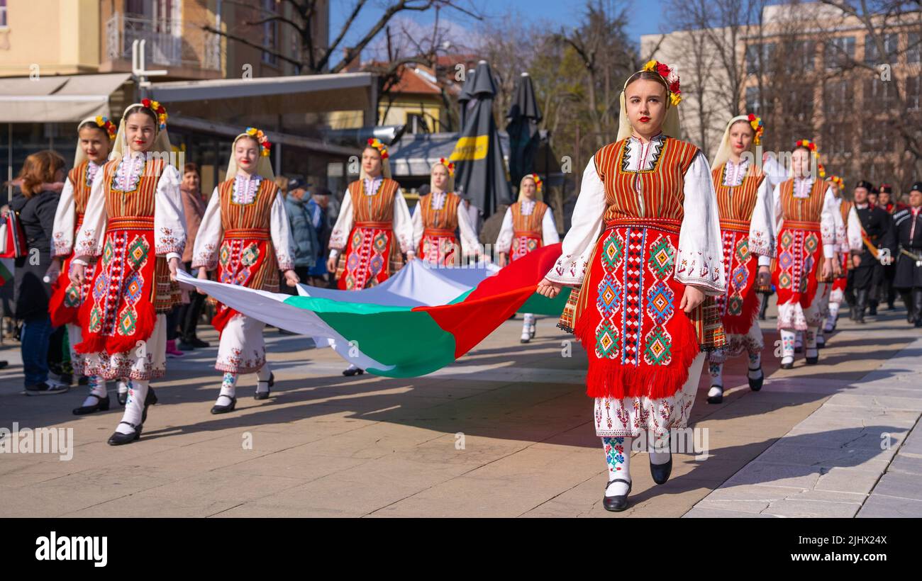 A Girls in Bulgarian traditional dresses hold the Bulgarian flag in Military Parade Stock Photo
