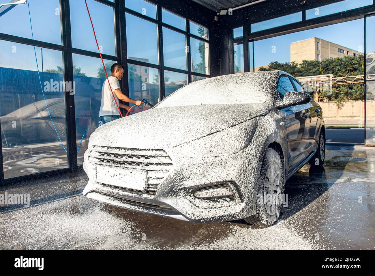 Selfservice car wash. A man waters his car with foam from a