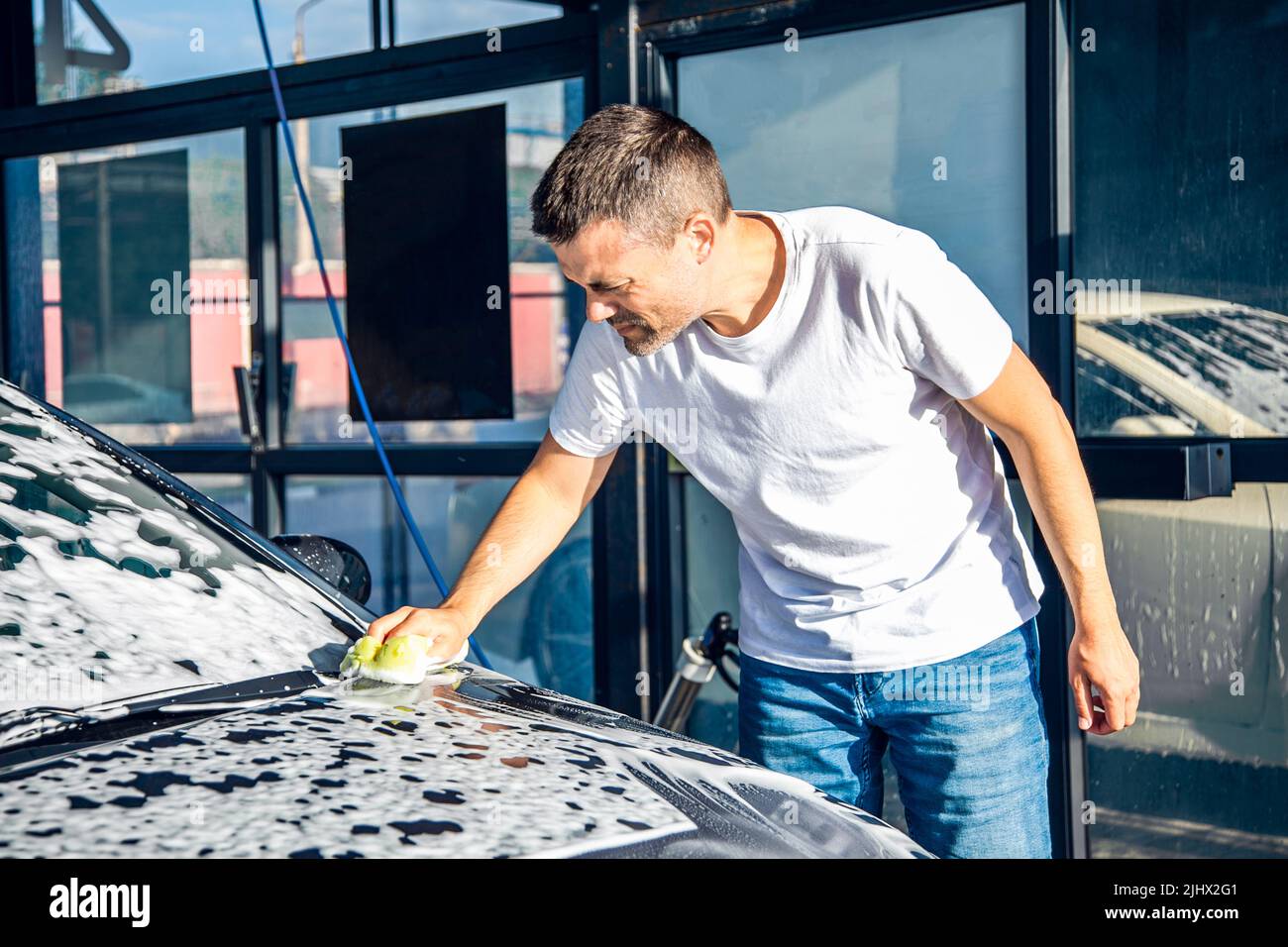 a-man-washes-his-car-with-foam-at-a-self-service-car-wash-stock-photo
