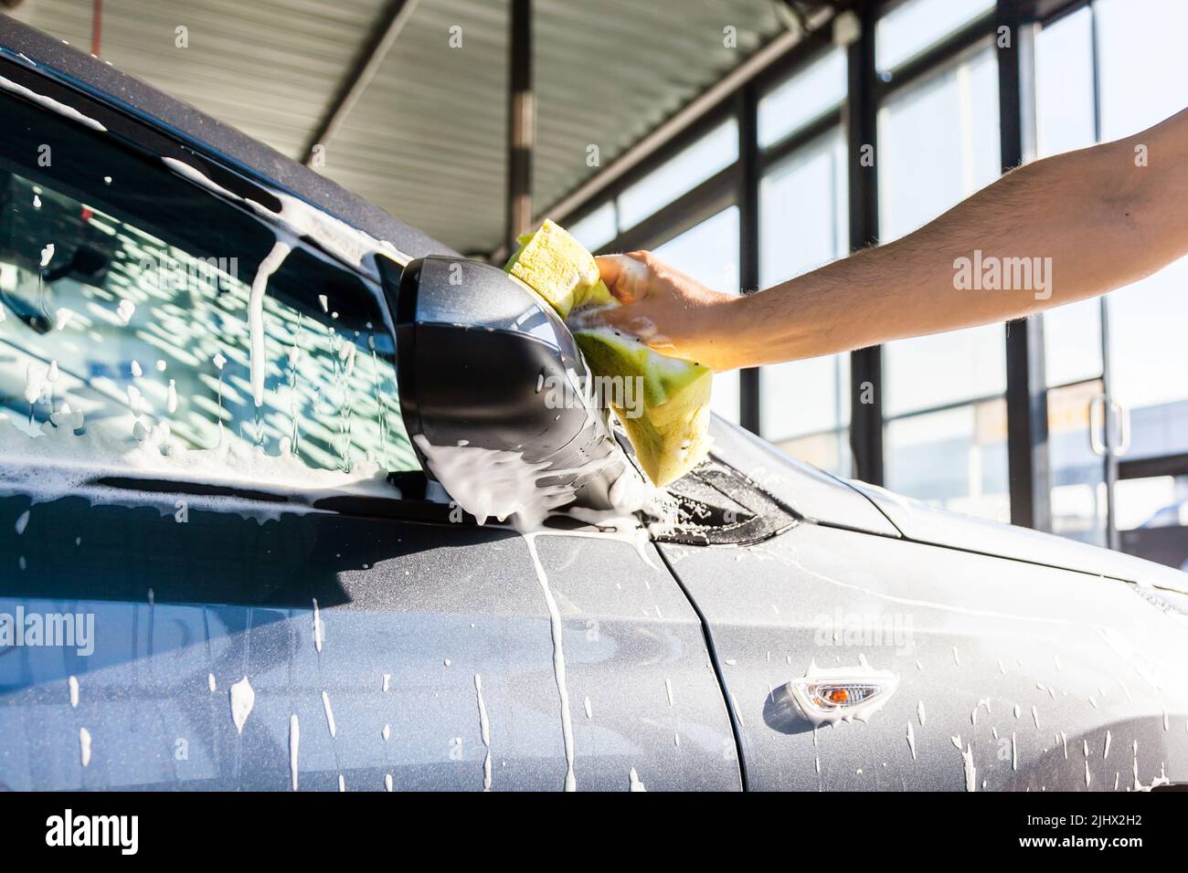 A man washes the mirror on his car with foam at a selfservice car wash, closeup Stock Photo