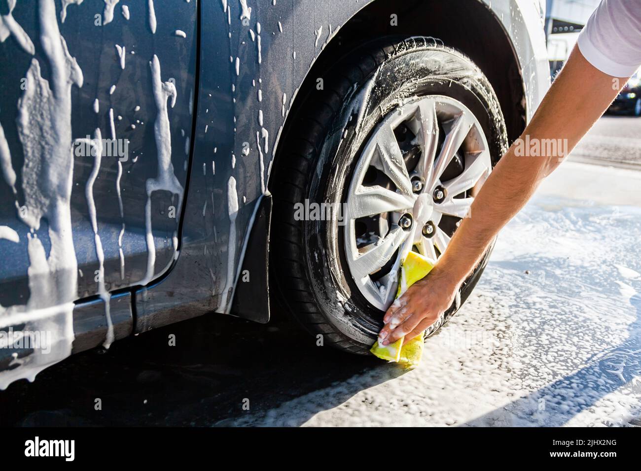 A man washes his car with foam at a selfservice car wash, wheels and